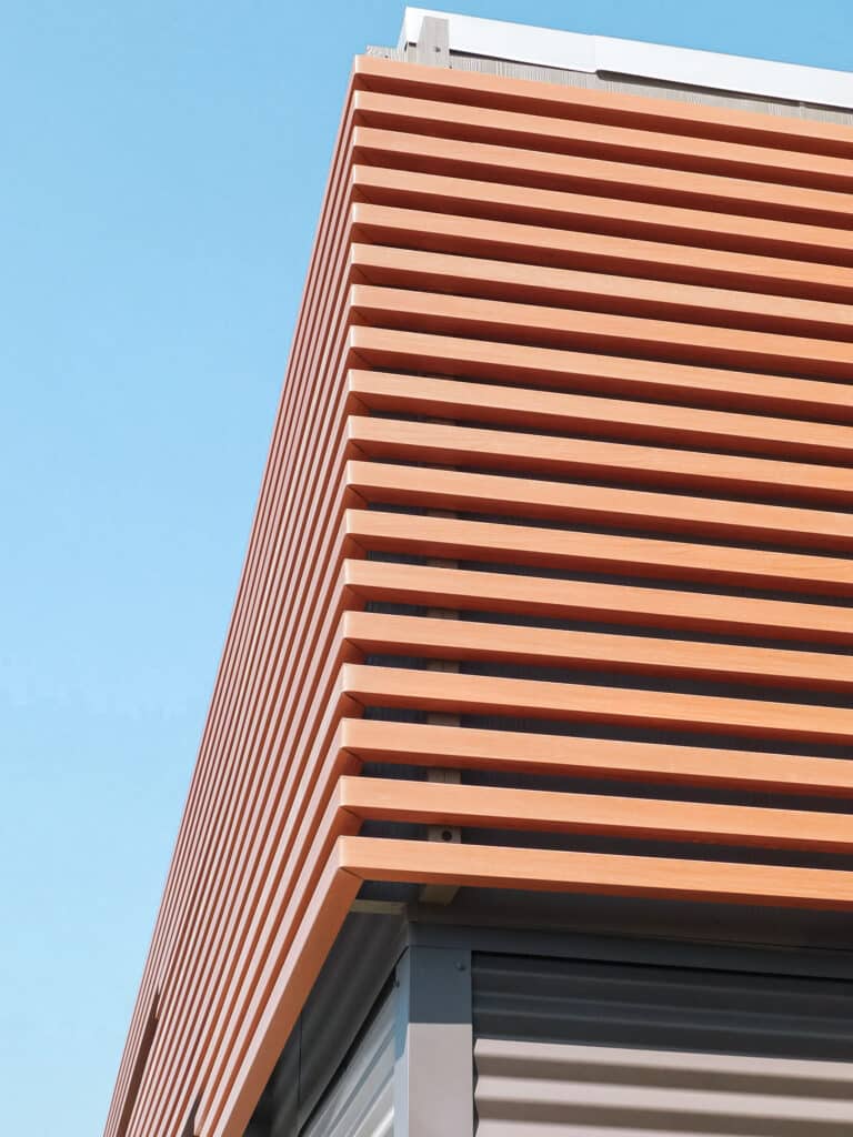 Modern building corner with wooden slats and blue sky.