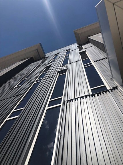 Tall building with vertical metal panels against sky.